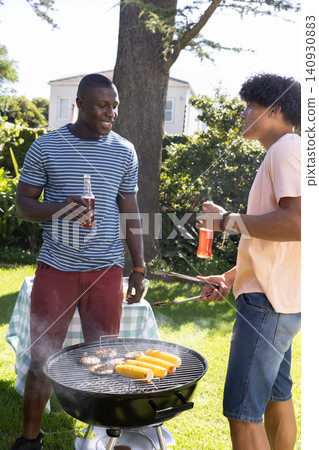Diverse friends barbecuing burgers, corn on cob at grill in backyard near checkered table Diverse friends barbecuing burgers, corn on cob at grill in backyard near checkered table 140930883