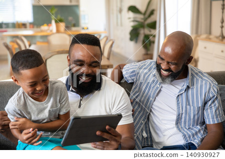 African American family sharing digital tablet and laughing on gray sofa in open-plan living area African American family sharing digital tablet and laughing on gray sofa in open-plan living area 140930927