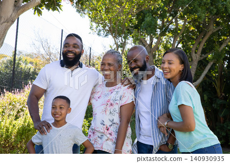 Diverse family standing together in shady backyard under trees with chain-link fence and shrubs 140930935