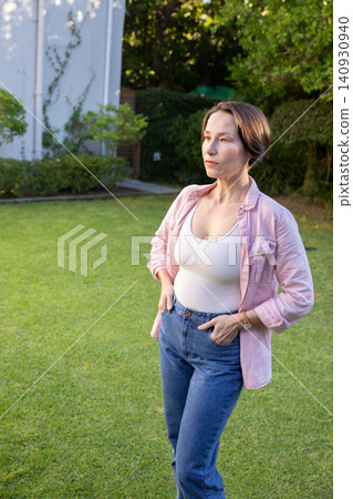 Mature woman standing on lawn by ivy-covered wall wearing wristwatch and jeans, copy space Mature woman standing on lawn by ivy-covered wall wearing wristwatch and jeans, copy space 140930940