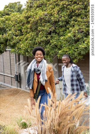 African american couple walking along front yard pulling silver suitcase carrying crossbody bag African american couple walking along front yard pulling silver suitcase carrying crossbody bag 140930958