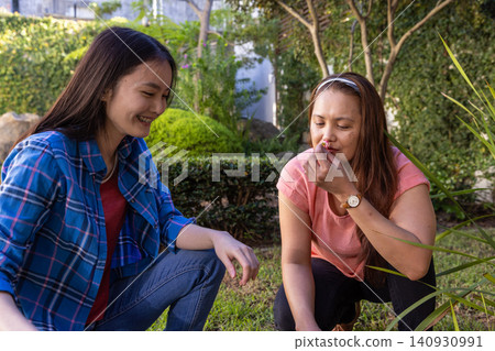 Asian mother and daughter gardening on grassy lawn smelling small blossom near trimmed hedges Asian mother and daughter gardening on grassy lawn smelling small blossom near trimmed hedges 140930991