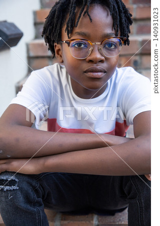 African american boy sitting on outdoor brick steps by wall wearing round glasses and t-shirt African american boy sitting on outdoor brick steps by wall wearing round glasses and t-shirt 140931023