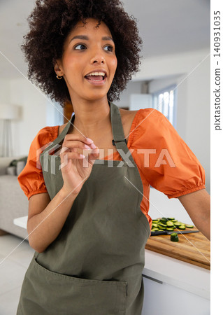 Woman chopping zucchini on cutting board at kitchen island wearing apron talking Woman chopping zucchini on cutting board at kitchen island wearing apron talking 140931035