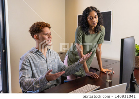 Diverse coworkers discussing project while pointing at computer monitor on wood desk in office Diverse coworkers discussing project while pointing at computer monitor on wood desk in office 140931041