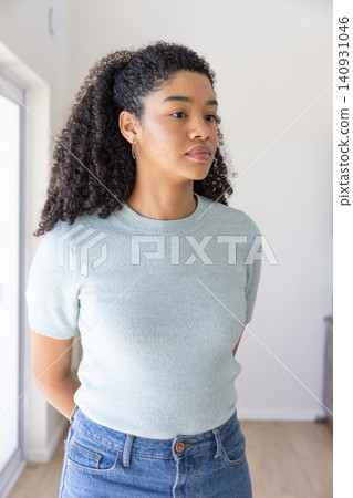 African american woman standing in sunlit home wearing blue sweater, jeans next to window sensor African american woman standing in sunlit home wearing blue sweater, jeans next to window sensor 140931046