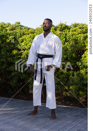 African american man practicing martial arts stance wearing white gi and black belt on deck African american man practicing martial arts stance wearing white gi and black belt on deck 140931053