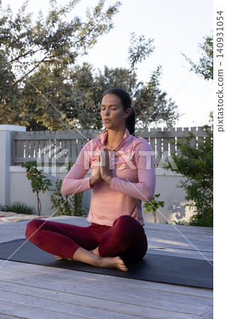 Woman sitting on yoga mat on backyard deck, meditating in prayer position Woman sitting on yoga mat on backyard deck, meditating in prayer position 140931054