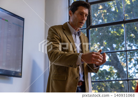 Adult male in tan blazer presenting spreadsheet near window in meeting room Adult male in tan blazer presenting spreadsheet near window in meeting room 140931068