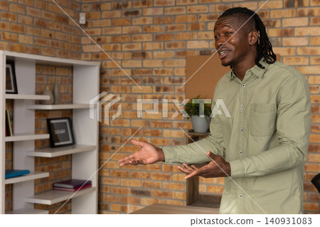 African american man gesturing, speaking in office in green shirt next to open shelf, copy space African american man gesturing, speaking in office in green shirt next to open shelf, copy space 140931083
