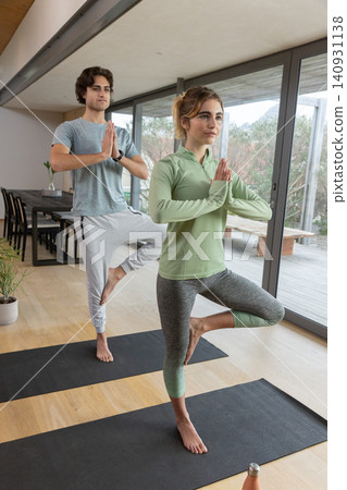 Couple practicing yoga in tree pose on black mats in modern home living and dining space Couple practicing yoga in tree pose on black mats in modern home living and dining space 140931138