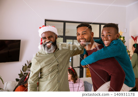 African american family celebrating christmas at home in santa hat, dad carrying boy piggyback African american family celebrating christmas at home in santa hat, dad carrying boy piggyback 140931178