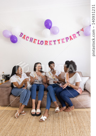 Diverse female friends wearing sashes toasting champagne flutes at home for bachelorette party Diverse female friends wearing sashes toasting champagne flutes at home for bachelorette party 140931231