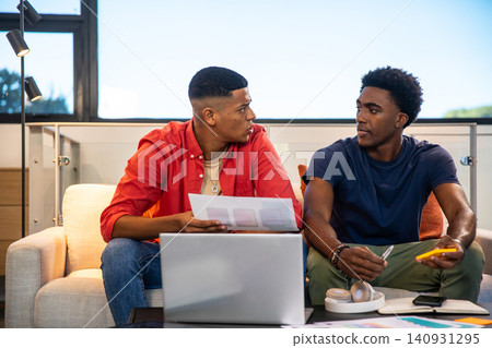 Diverse male colleagues collaborating in lounge reviewing documents and smartphone on coffee table Diverse male colleagues collaborating in lounge reviewing documents and smartphone on coffee table 140931295