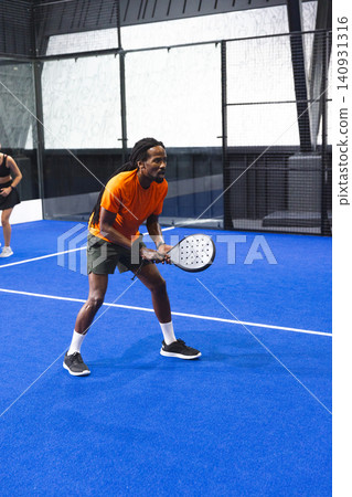 Diverse sports partners in sportswear practicing padel and holding rackets on synthetic turf court Diverse sports partners in sportswear practicing padel and holding rackets on synthetic turf court 140931316