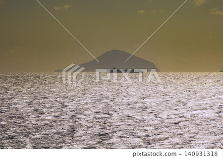 暮色漸濃,在大海上,大島和一艘貨櫃船的輪廓在近海地平線上清晰可見。 暮色漸濃,在大海上,大島和一艘貨櫃船的輪廓在近海地平線上清晰可見。 140931318