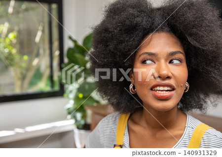 African American woman sitting by large window at home, speaking in striped shirt with gold hoops African American woman sitting by large window at home, speaking in striped shirt with gold hoops 140931329