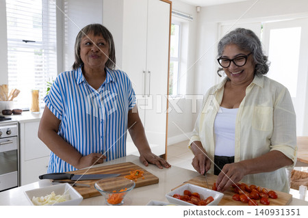 Senior women wearing button-up shirts preparing salad in kitchen with wooden boards and knife Senior women wearing button-up shirts preparing salad in kitchen with wooden boards and knife 140931351