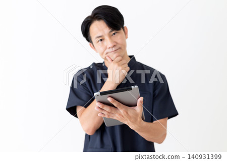 一位身穿藏藍色手術服的中年男醫生正看著平板電腦,陷入沉思。 一位身穿藏藍色手術服的中年男醫生正看著平板電腦,陷入沉思。 140931399