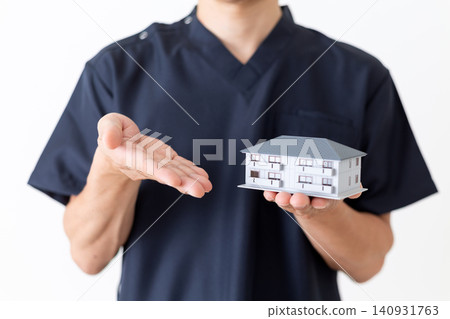 一位身穿藏藍色手術服的中年男醫生向人推薦了一套樣品屋。 一位身穿藏藍色手術服的中年男醫生向人推薦了一套樣品屋。 140931763