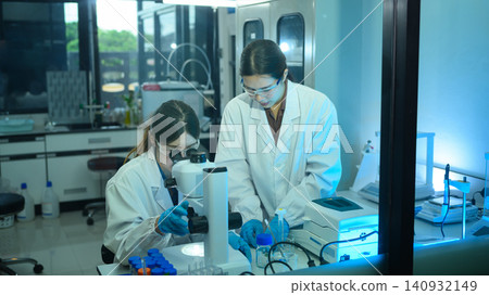 Two Female Scientists Working Together in Modern Research Laboratory with Microscope and Equipment Two Female Scientists Working Together in Modern Research Laboratory with Microscope and Equipment 140932149