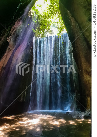 Cave waterfall viewed from inside rocky grotto with light rays filtering through jungle canopy opening above Cave waterfall viewed from inside rocky grotto with light rays filtering through jungle canopy opening above 140932219