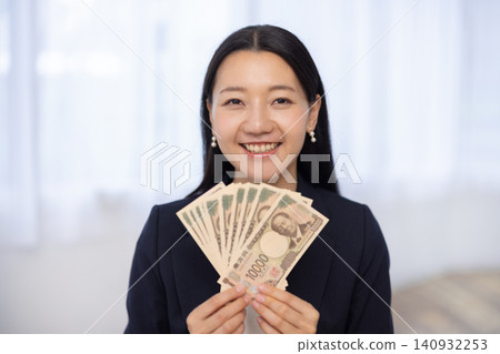 A young Japanese businesswoman smiles at the camera, holding ten 10,000 yen bills. A young Japanese businesswoman smiles at the camera, holding ten 10,000 yen bills. 140932253