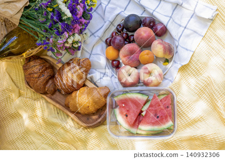 Picnic spread with pastries fruit and flowers on yellow blanket Picnic spread with pastries fruit and flowers on yellow blanket 140932306