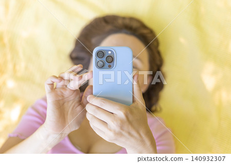 Woman lying down using smartphone in light blue case top view Woman lying down using smartphone in light blue case top view 140932307