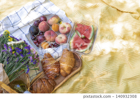 Picnic Spread with Fresh Fruit Croissants and Flowers on Yellow Blanket Picnic Spread with Fresh Fruit Croissants and Flowers on Yellow Blanket 140932308