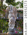 Classical white angel statue with wings in a garden courtyard with bougainvillea and Mediterranean-style building 140932573