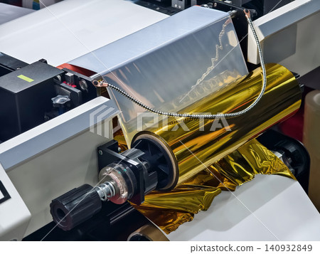Machine applies gold foil to paper in a production facility during working hours 140932849