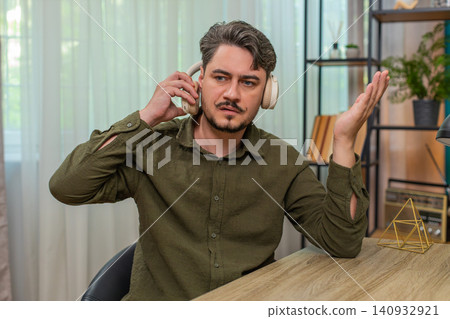 Middle-aged man lifts headphones sighs sad after bad audio news feeling disappointed at table desk Middle-aged man lifts headphones sighs sad after bad audio news feeling disappointed at table desk 140932921