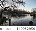 A view of the lake at dawn through tree branches, with catamarans moored. The city's waterfront with boats at dusk. 140932950