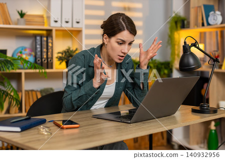 Young woman on home table feeling angry at laptop while struggling to solve problem during work time Young woman on home table feeling angry at laptop while struggling to solve problem during work time 140932956