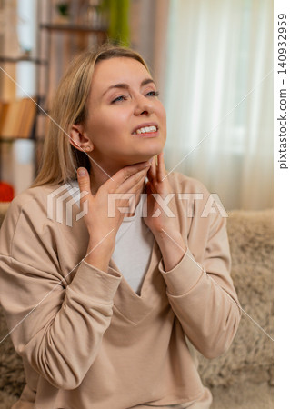 Adult woman touching throat at home, showing sore pain and discomfort while swallowing on home sofa Adult woman touching throat at home, showing sore pain and discomfort while swallowing on home sofa 140932959