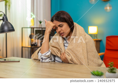 Indian woman wrapped in blanket touches forehead checking temperature feeling worried fever indoors Indian woman wrapped in blanket touches forehead checking temperature feeling worried fever indoors 140932975