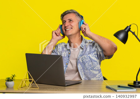 Man in wireless headphones working on laptop at table nodding head enjoying favorite music sound Man in wireless headphones working on laptop at table nodding head enjoying favorite music sound 140932997