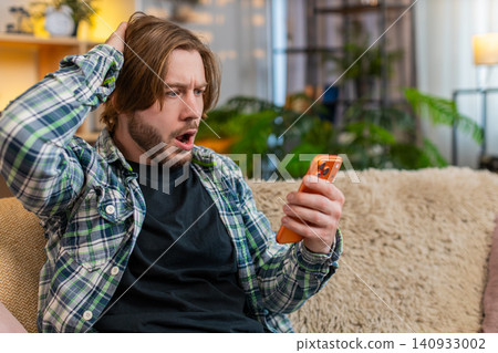 Young man on home sofa upset after poor smartphone result feeling defeat and stress in living room 140933002