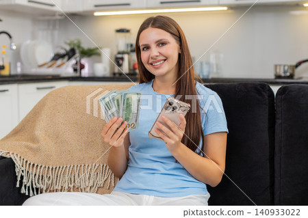 Young woman counts dollars money cash with smartphone checks exchange rate plans purchase invests Young woman counts dollars money cash with smartphone checks exchange rate plans purchase invests 140933022