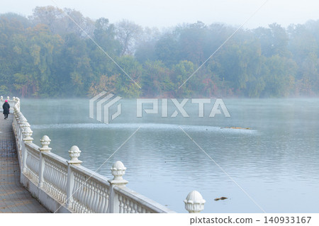 Misty October morning walk along a waterfront promenade beside a calm river Misty October morning walk along a waterfront promenade beside a calm river 140933167