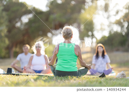 Senior woman leading outdoor yoga and meditation class Senior woman leading outdoor yoga and meditation class 140934244