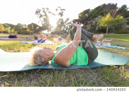 Senior woman practicing outdoor group yoga for wellness Senior woman practicing outdoor group yoga for wellness 140934265