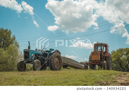 Two tractors stand in a bright green field under a cloudy sky Two tractors stand in a bright green field under a cloudy sky 140934283