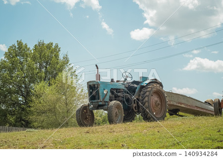 A vintage tractor pulls a trailer with a boat across a sunny rural field against a blue sky. High quality photoA blue vintage tractor pulls a trailer loaded with a boat across a green field under a br A vintage tractor pulls a trailer with a boat across a sunny rural field against a blue sky. High quality photoA blue vintage tractor pulls a trailer loaded with a boat across a green field under a br 140934284