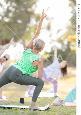 Senior woman practicing yoga pose outdoors with group Senior woman practicing yoga pose outdoors with group 140934324