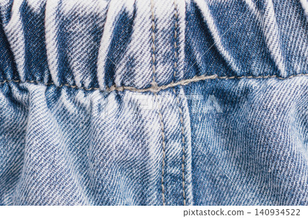 Horizontal close up shot of a blue denim jeans fabric texture with an elastic waistband gather and detailed double stitching line on a classic cotton material Horizontal close up shot of a blue denim jeans fabric texture with an elastic waistband gather and detailed double stitching line on a classic cotton material 140934522