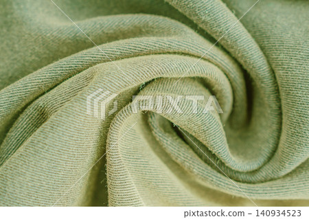 Horizontal close up macro shot of a soft olive green cotton fabric texture folded in a spiral shape with detailed diagonal weave pattern under soft light 140934523