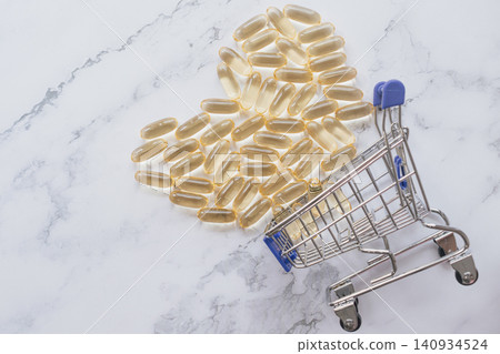 Horizontal high angle shot of golden omega fish oil capsules arranged in a heart shape with a small shopping cart on a white marble background under bright light Horizontal high angle shot of golden omega fish oil capsules arranged in a heart shape with a small shopping cart on a white marble background under bright light 140934524