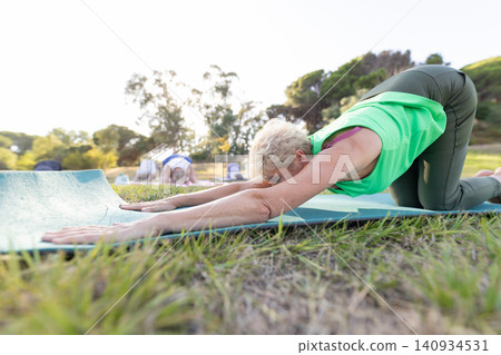 Senior woman practicing yoga in child's pose outdoors Senior woman practicing yoga in child's pose outdoors 140934531